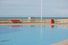 Enpty Childrens paddling pool with red bench and bin.